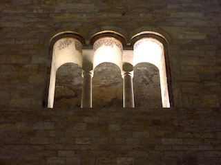 Three arched illuminated windows high in a wall